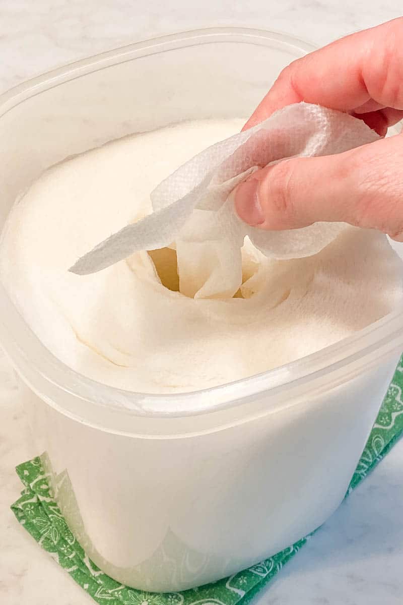 hand pulling homemade cleaning wipes made with paper towels out of clear plastic container