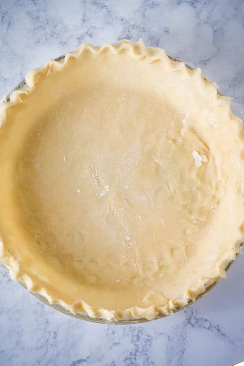 homemade pie crust in glass pie plate on white marble countertop