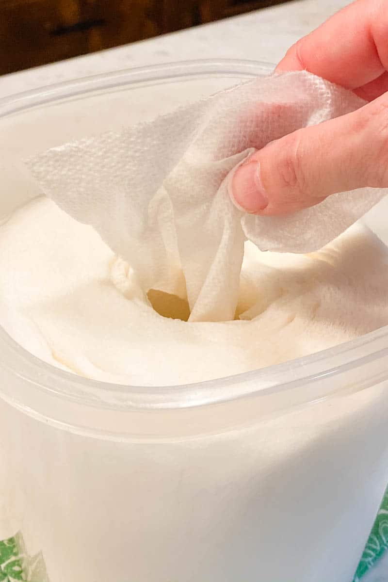 hand pulling natural cleaning wipes out of plastic sealable container