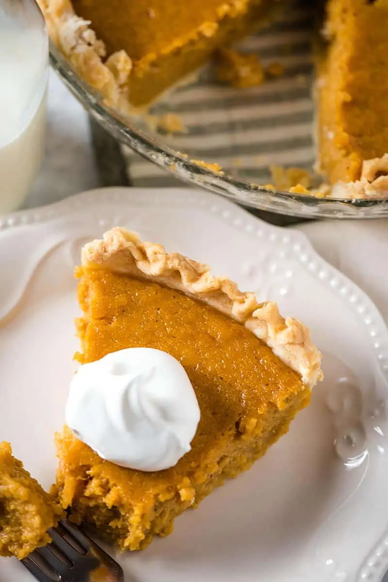 slice of sweet potato pie with homemade pie crust and whipped cream on white plate with fork