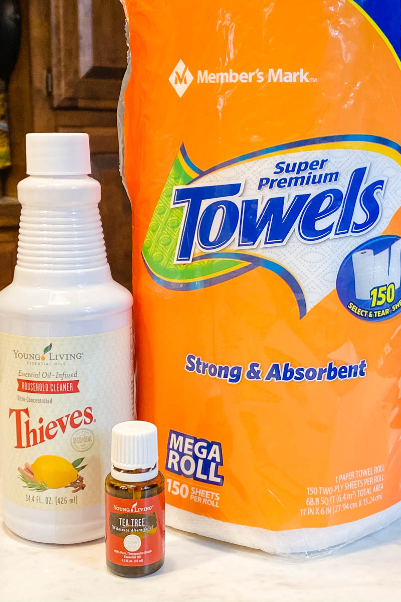 Thieves wipes ingredients, including paper towels, Thieves Household Cleaner, and Young Living Tea Tree oil on white countertop