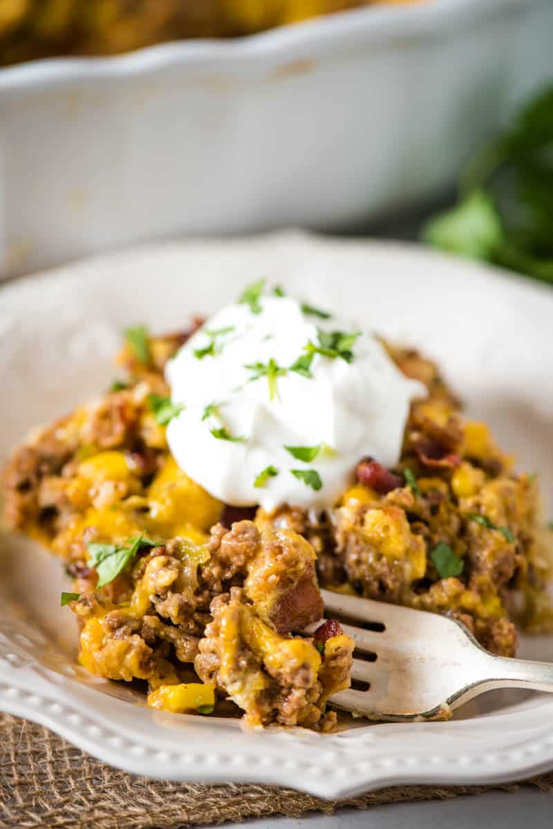 bite of taco pie on fork, from serving on white plate with sour cream and cilantro