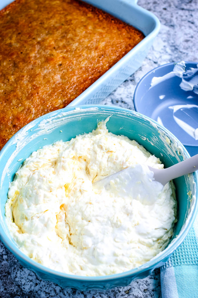easy pineapple cake in light blue cake pan with teal bowl of whipped pudding topping and spatula