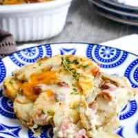 cheesy scalloped potatoes and ham on blue and white decorative plate on white linen