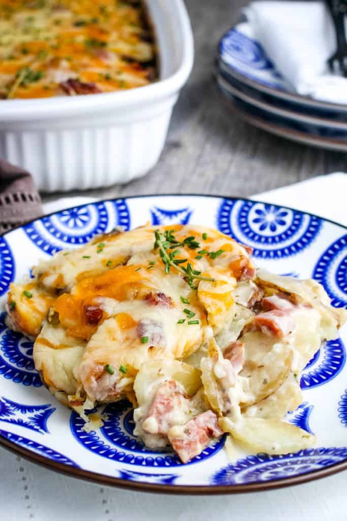cheesy scalloped potatoes and ham on blue and white decorative plate on white linen