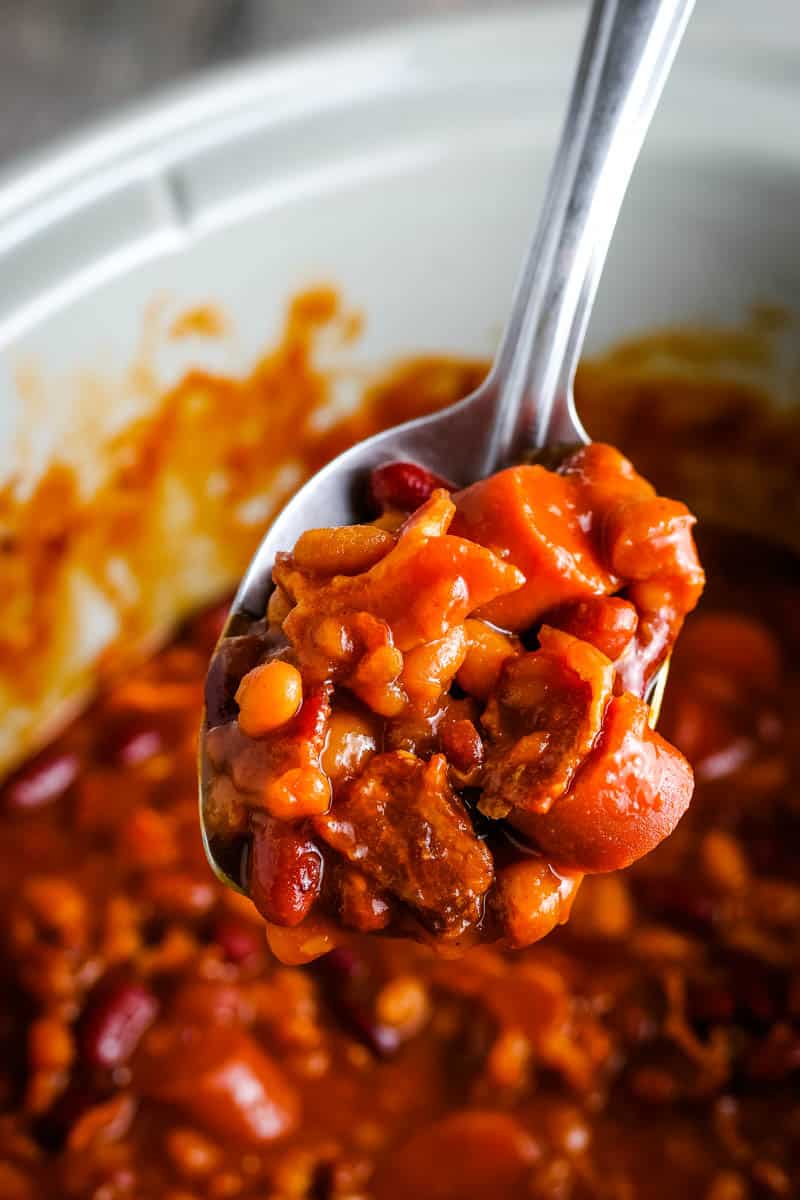 spoonful of CrockPot baked beans with bacon and hot dogs over gray slow cooker