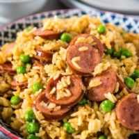 decorative blue bowl with Instant Pot sausage and rice, with green peas, sitting on wooden countertop on gray linen