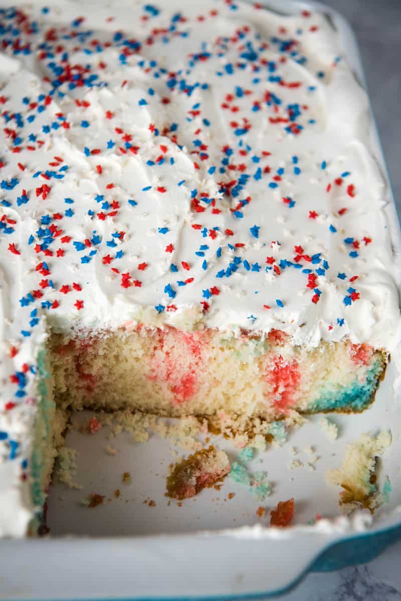 4th of July poke cake covered in whipped topping and mini star sprinkles, sliced in blue baking dish