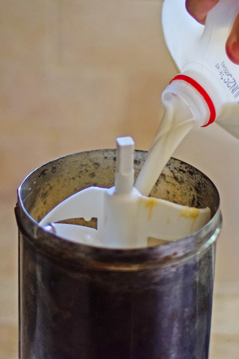 pouring whole milk into metal ice cream maker canister with white churning paddle