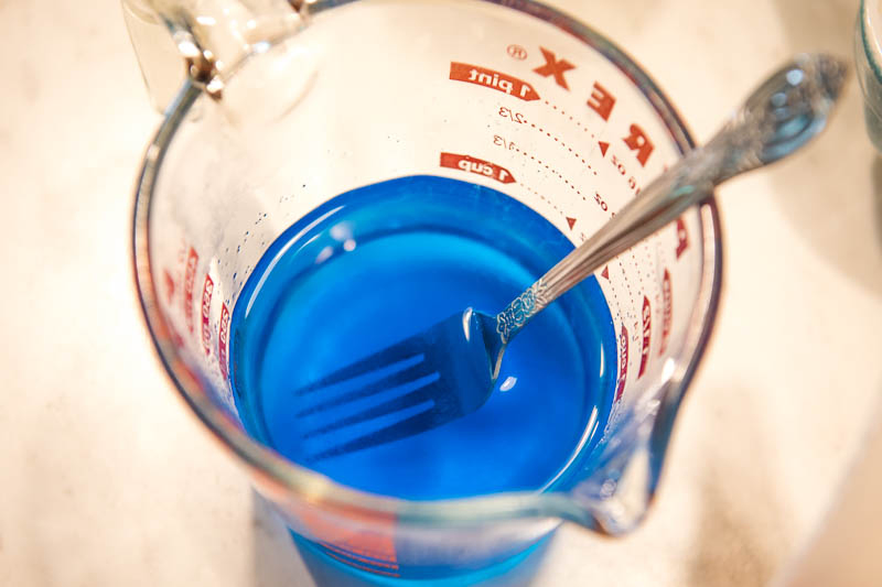 stirring berry blue Jello in glass Pyrex measuring cup with fork