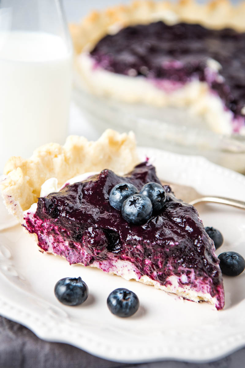 slice of blueberry cream cheese pie with blueberries on top on white plate with fork
