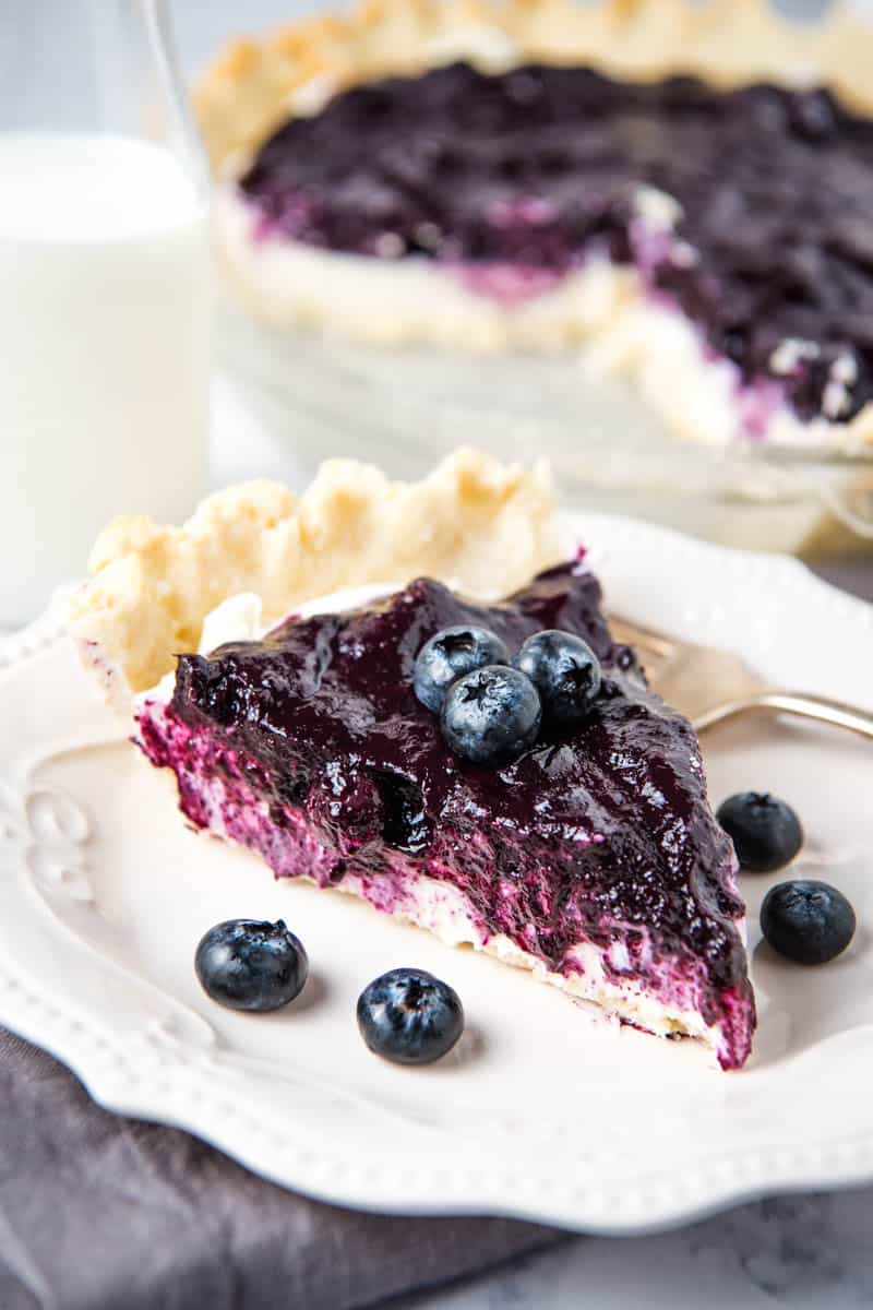 slice of blueberry cream pie on white plate with fresh blueberries and a fork