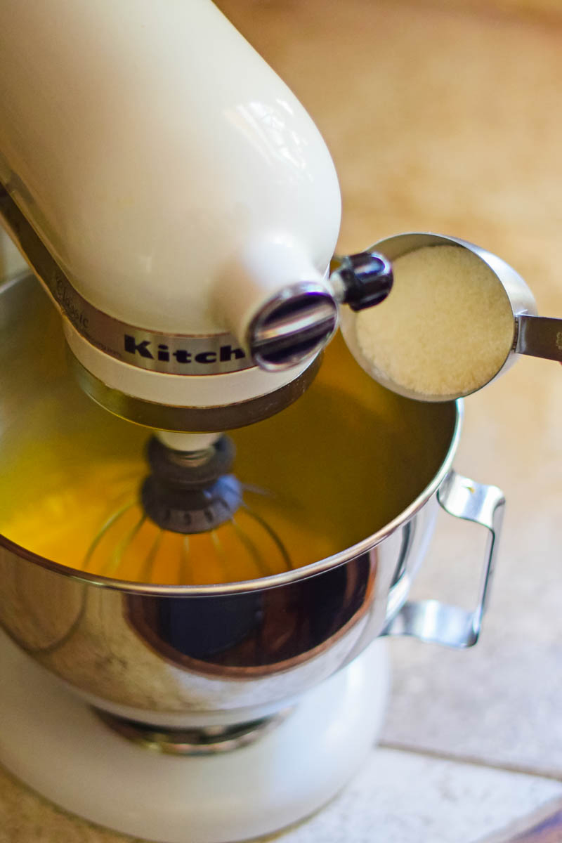 adding sugar to eggs in metal bowl of white KitchenAid mixer