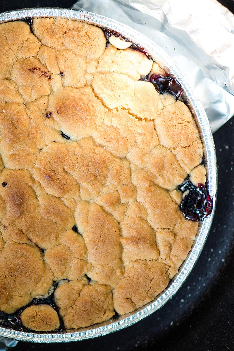 baked Dutch oven blueberry cobbler with sugar cookie topping in foil pan, down inside Dutch oven