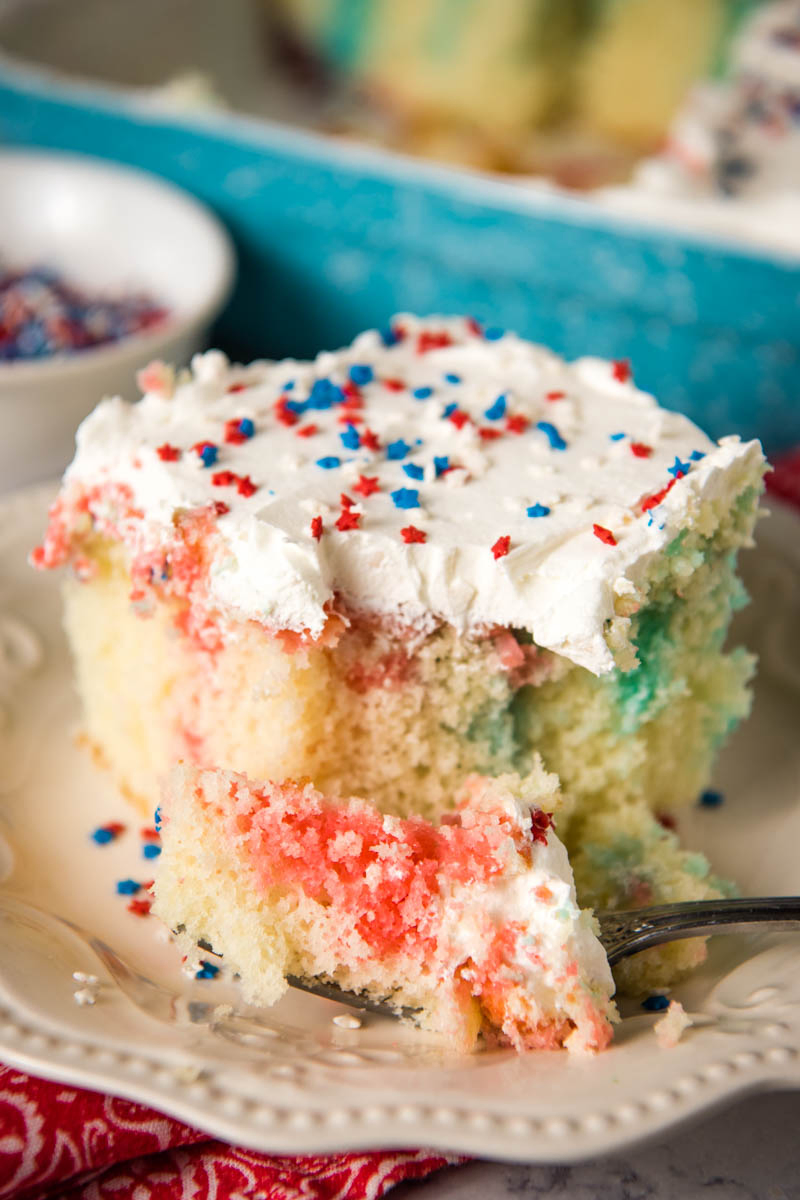 red white and blue Fourth of July poke cake with bite taken out with fork on white plate