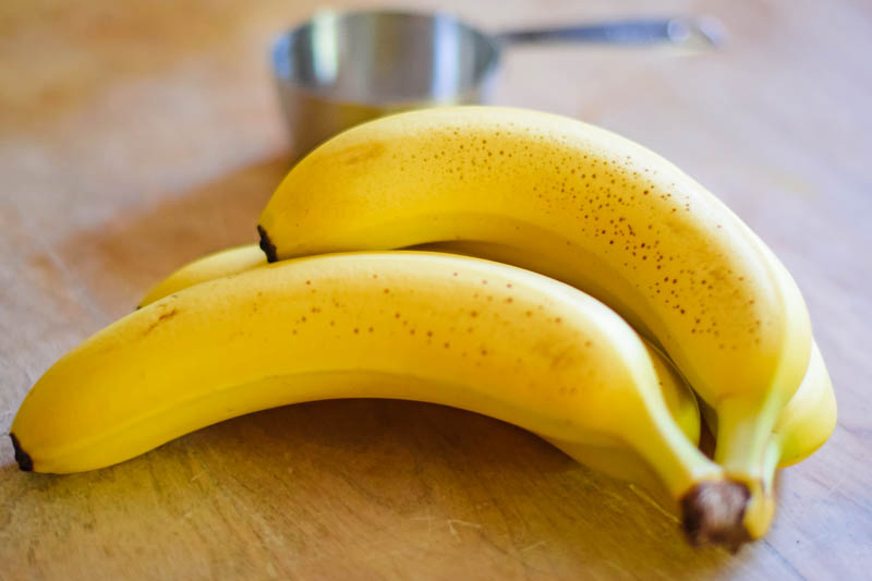 bunch of fresh bananas laying on wooden countertop with measuring cup