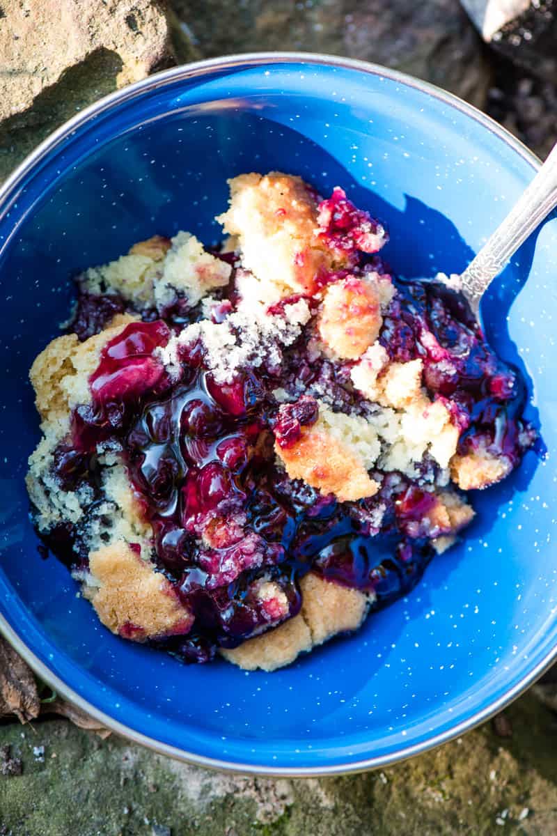 old-fashioned blueberry cobbler in blue enamel camping bowl with spoon
