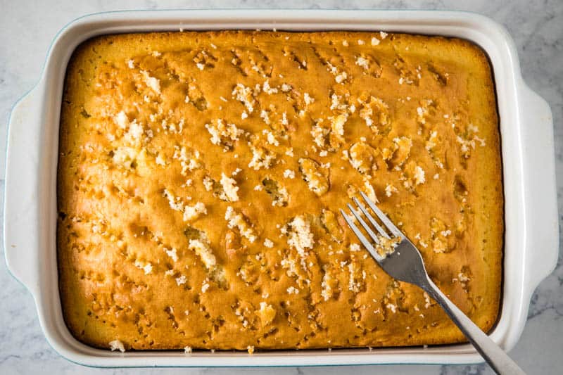 poking poke cake with fork in 9x13 baking dish