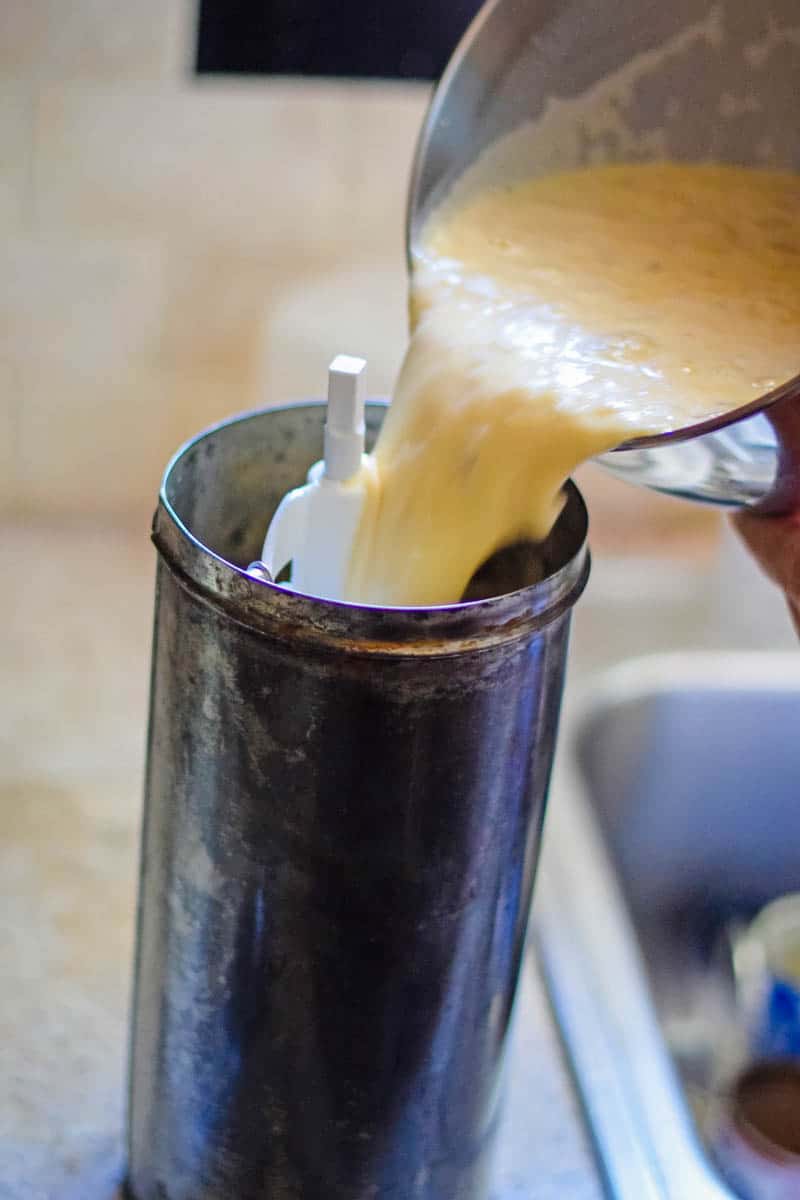 pouring banana ice cream mixture from metal bowl into metal ice cream canister with churning paddle