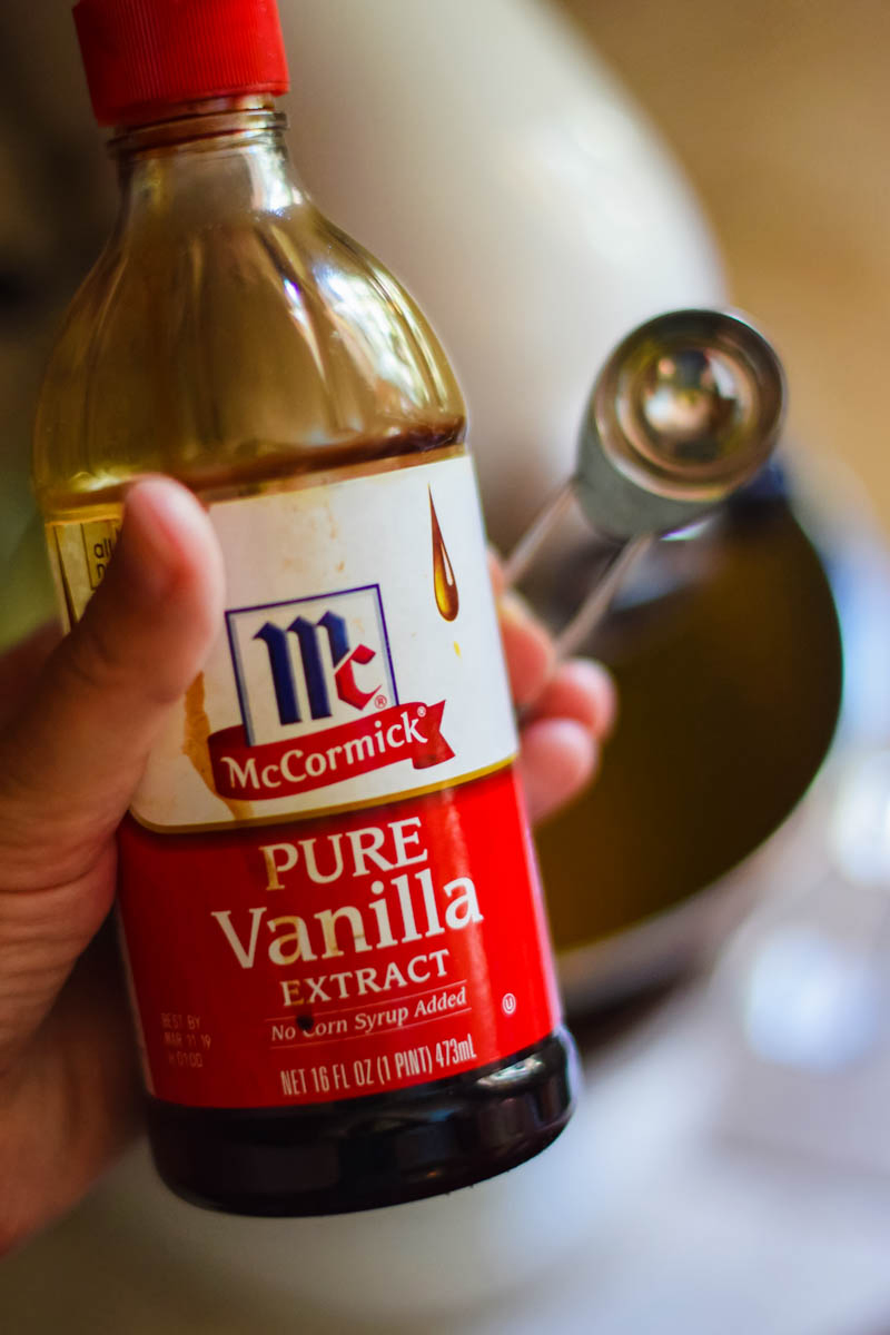 hand holding bottle of McCormick Pure Vanilla Extract with teaspoon