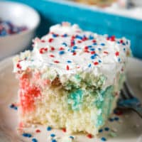 slice of red white and blue poke cake with whipped cream and sprinkles on white plate with fork