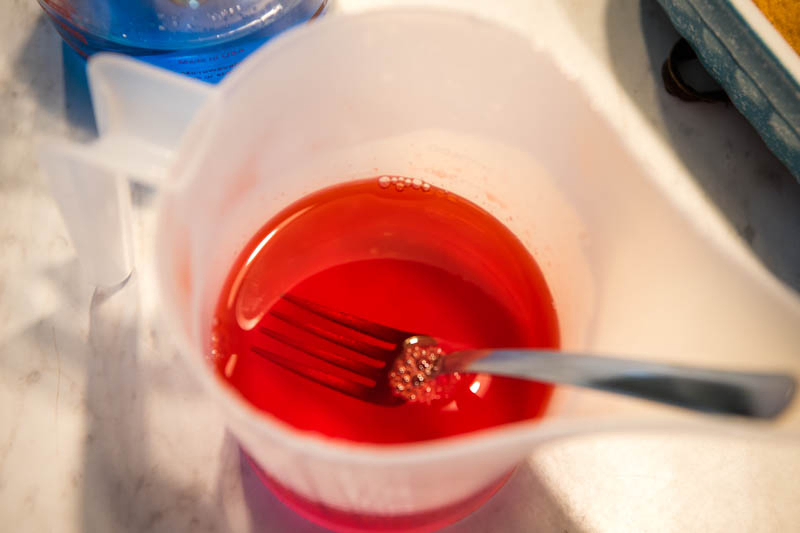 stirring red strawberry Jello in funnel pitcher with fork