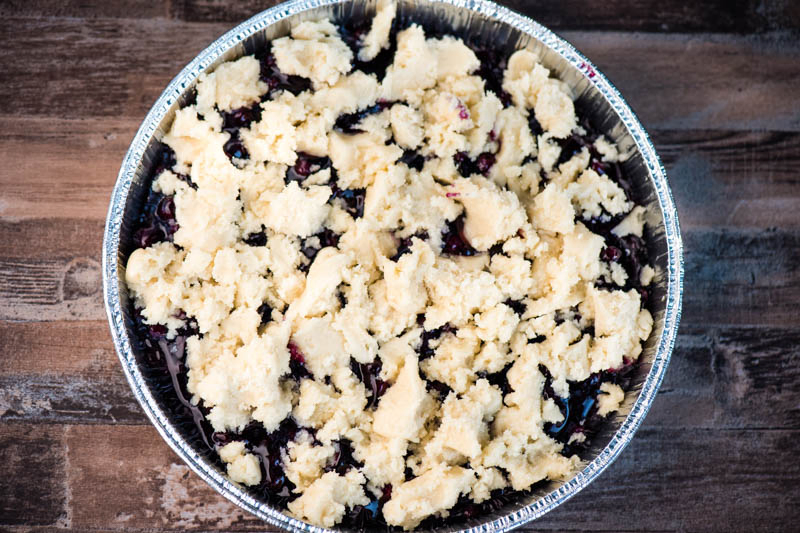 sugar cookie topping crumbled over blueberry pie filling in round foil pan