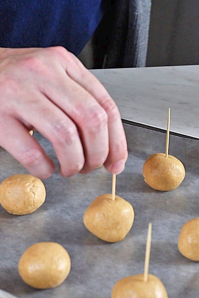 hand adding toothpicks to peanut butter balls for dipping