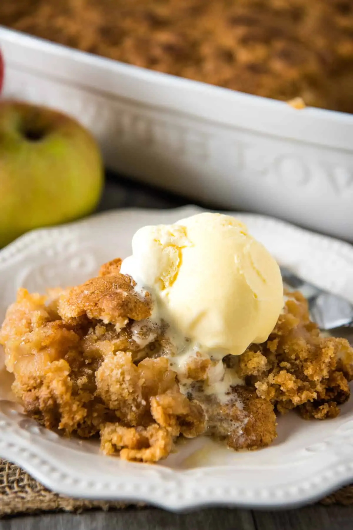 serving of apple crumble without oats, with scoop of vanilla ice cream on white plate with fork