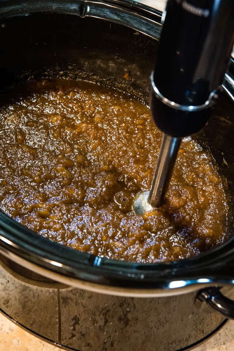 blending up slow cooker apple butter with immersion blender right in black CrockPot slow cooker