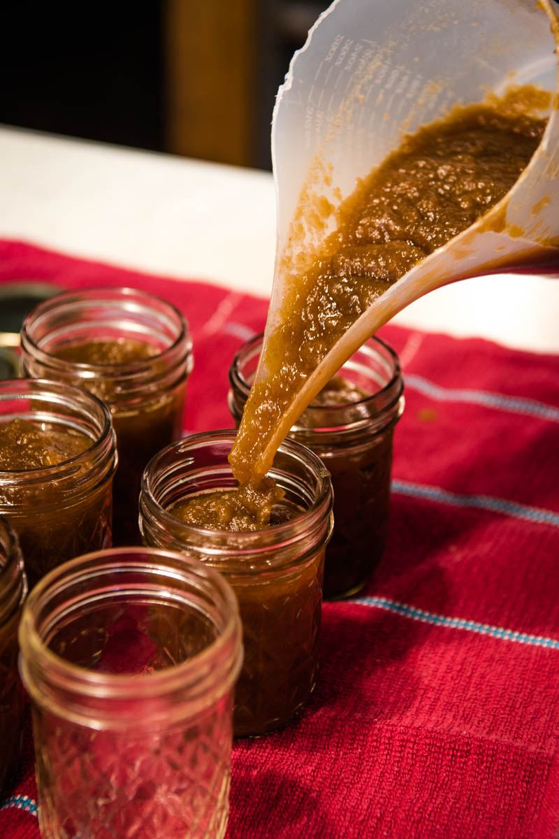pouring CrockPot apple butter into 8-ounce jelly jars for canning