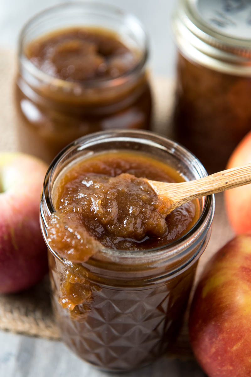 tiny wooden spoon in jar of CrockPot apple butter with apple butter dripping down side of jar