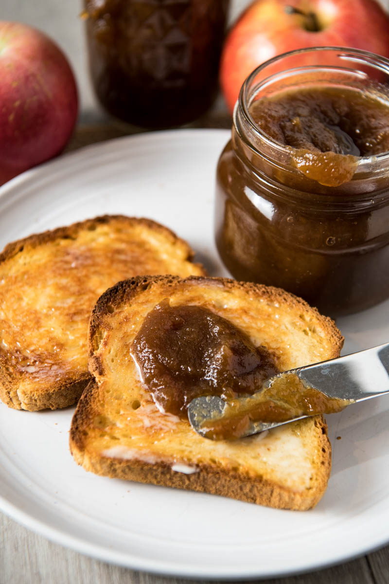 spreading homemade apple butter on toast with butter knife, on gray plate