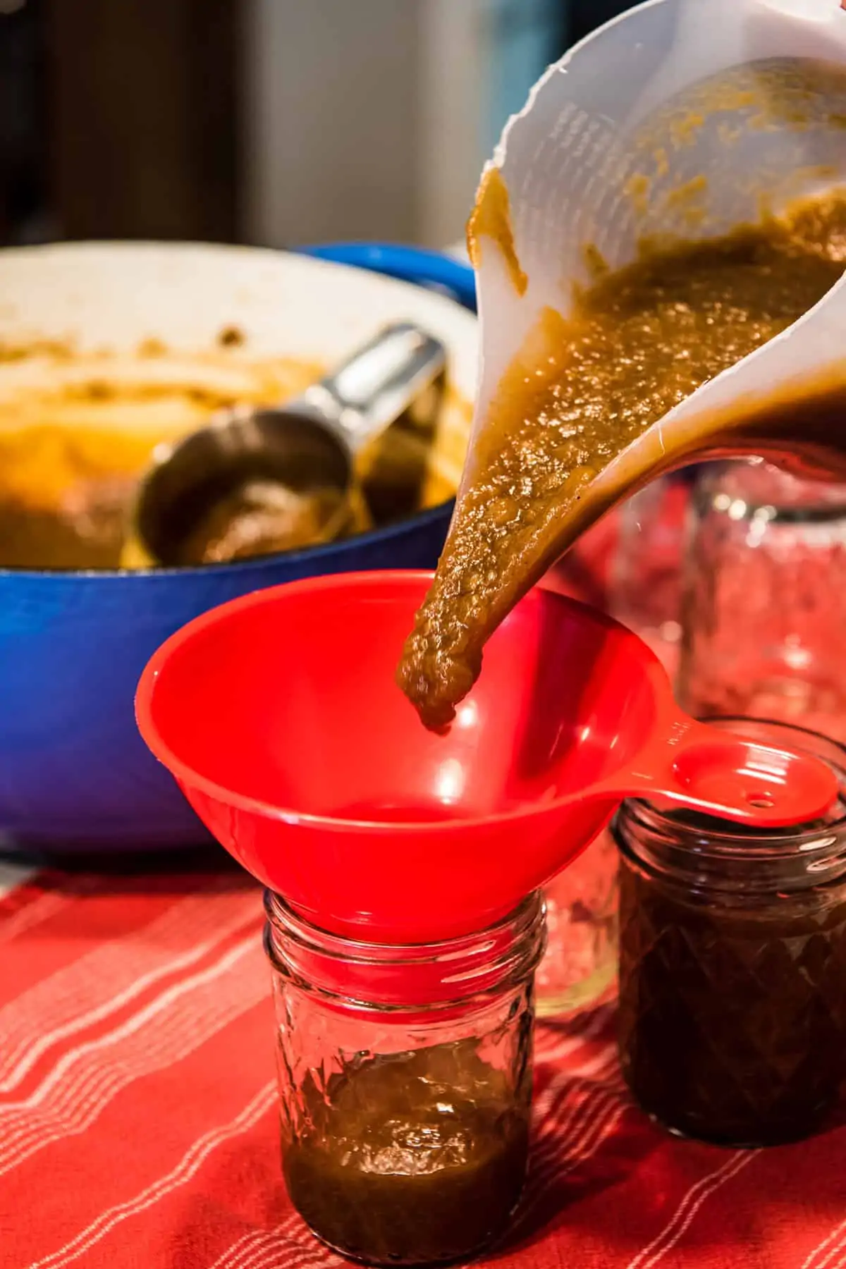 pouring easy stovetop apple butter from funnel pitcher into jelly jar using red jar funnel and funnel pitcher