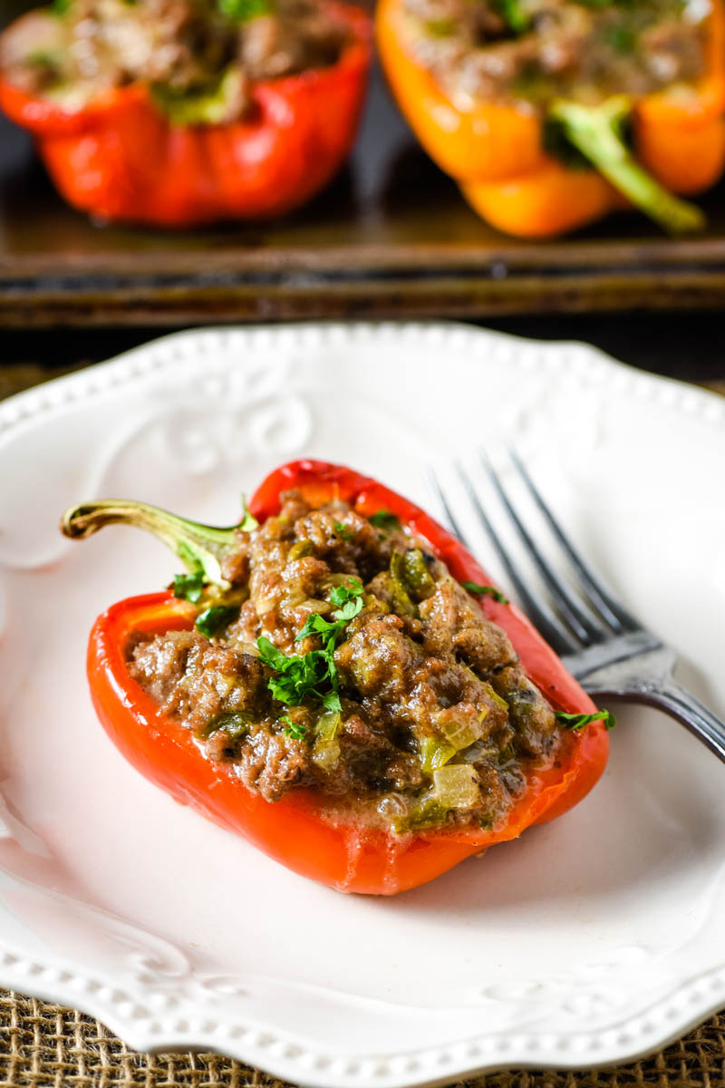red Philly cheesesteak stuffed pepper with ground beef, sprinkled with parsley, on white plate with fork