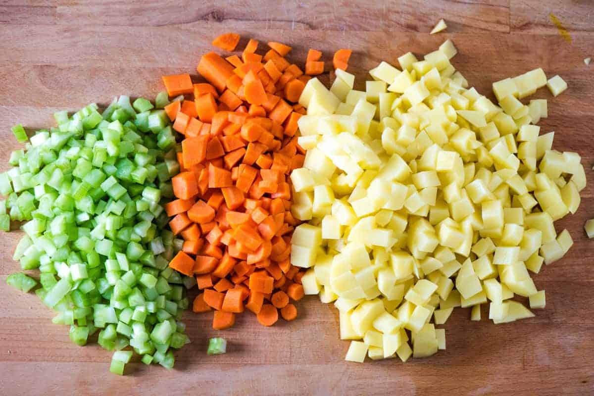 chopped fresh celery, carrots, and potatoes for hearty vegetable soup on wooden cutting board