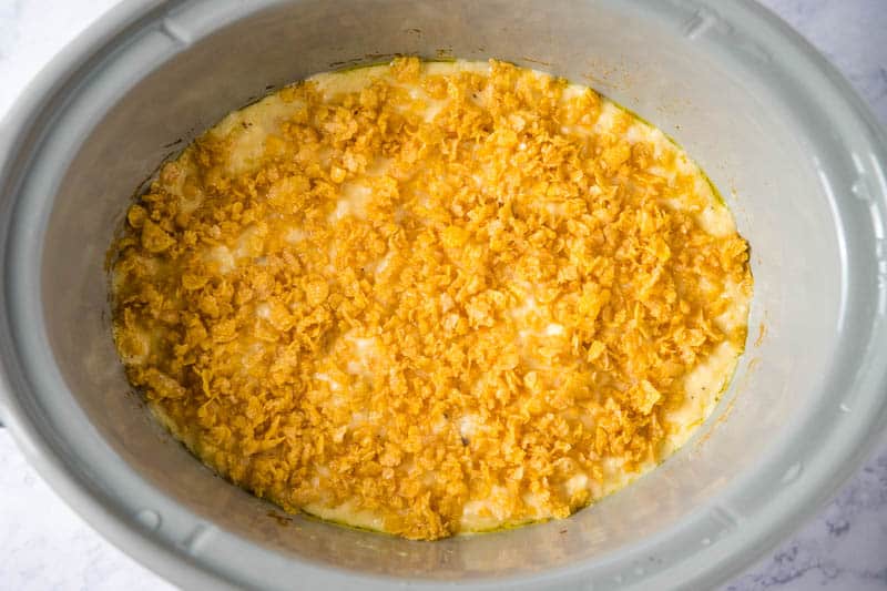 slightly crushed Corn Flakes sprinkled on top of hash brown casserole in gray slow cooker