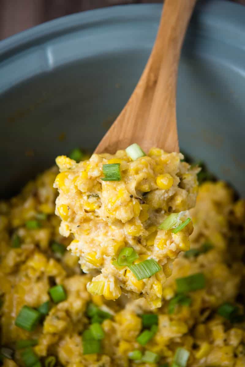scoop of Crock Pot corn pudding on wooden spoon over gray slow cooker