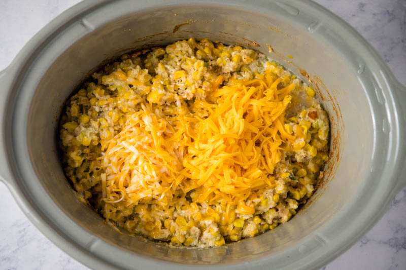 grated cheddar cheese on top of CrockPot corn casserole in gray slow cooker