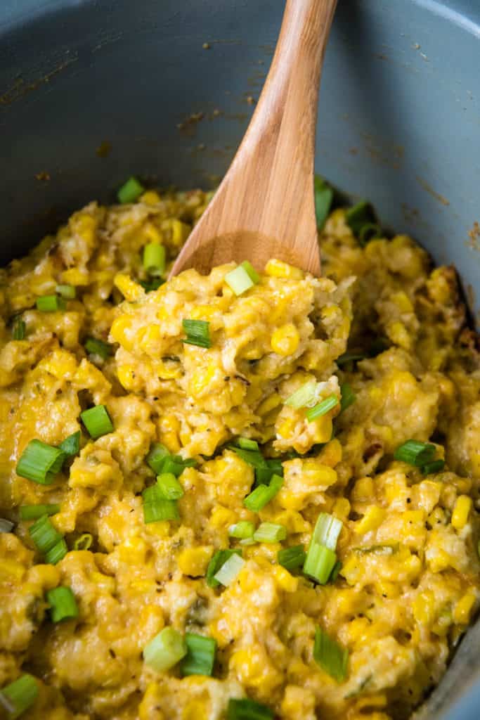 wooden spoon scooping CrockPot corn casserole out of gray slow cooker