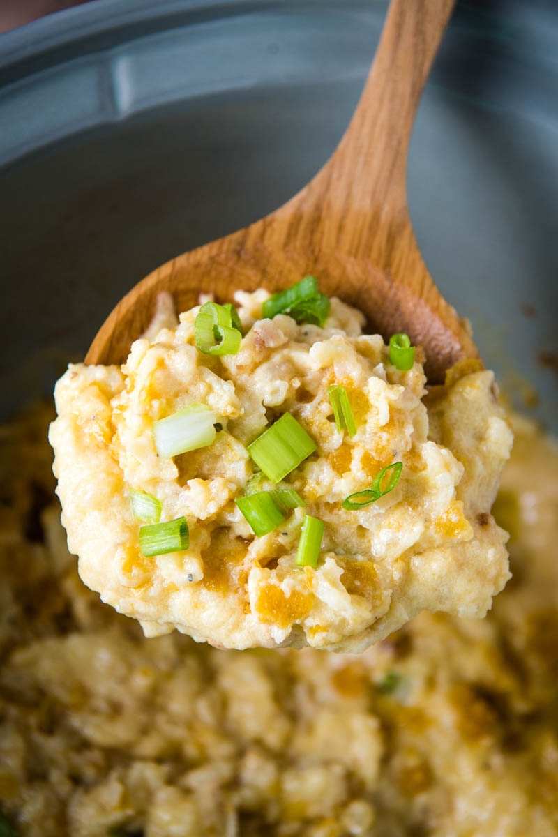 wooden spoonful of CrockPot funeral potatoes hash brown casserole, sprinkled with green onions, over gray slow cooker side dish