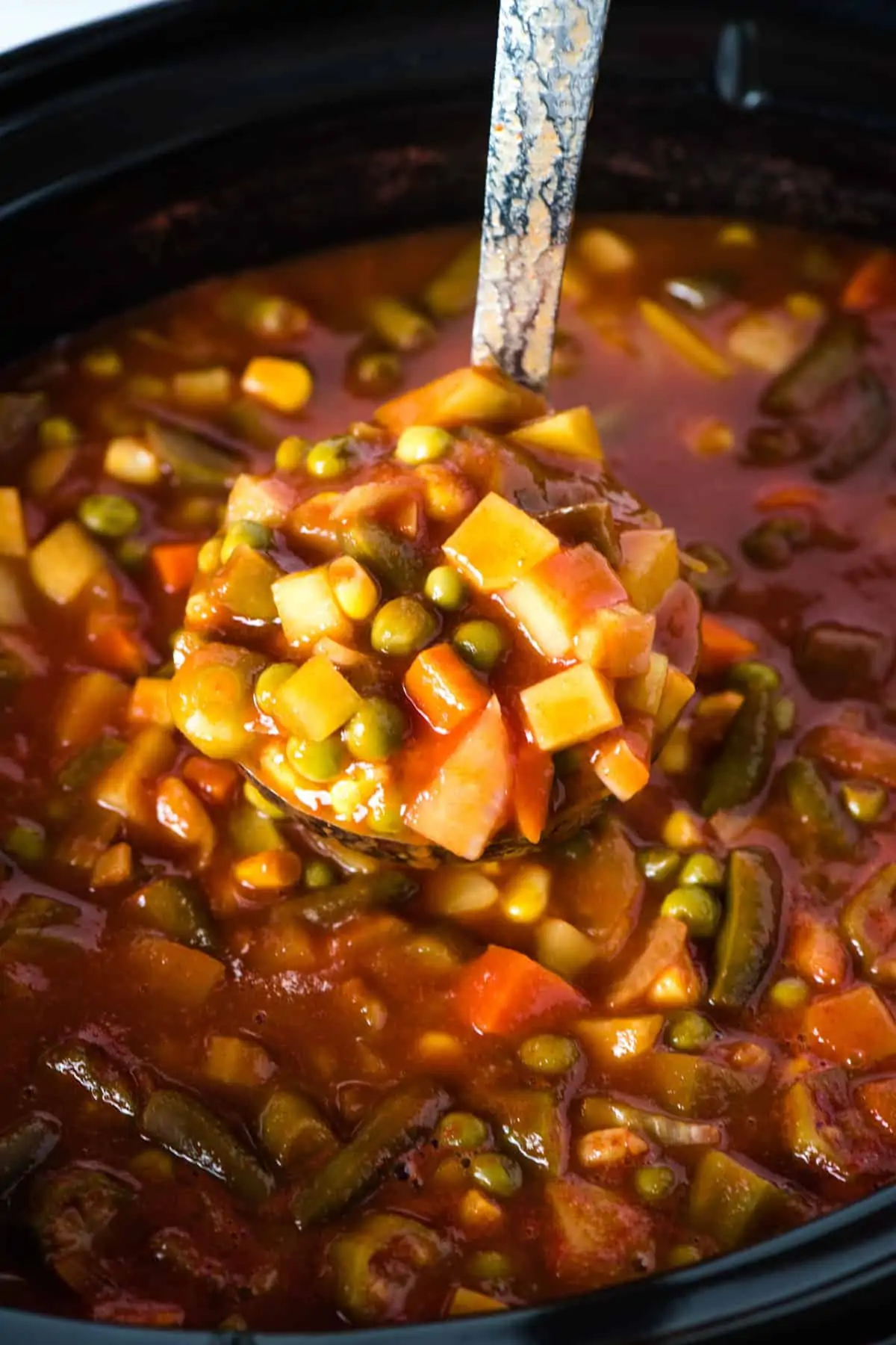 ladle full of CrockPot vegetable soup over black slow cooker full of soup