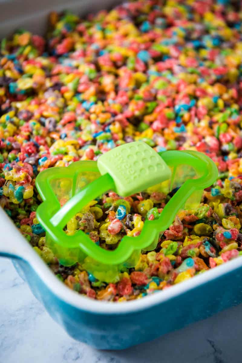 cutting Fruity Pebble treats out of blue baking dish with green Christmas tree cookie cutter