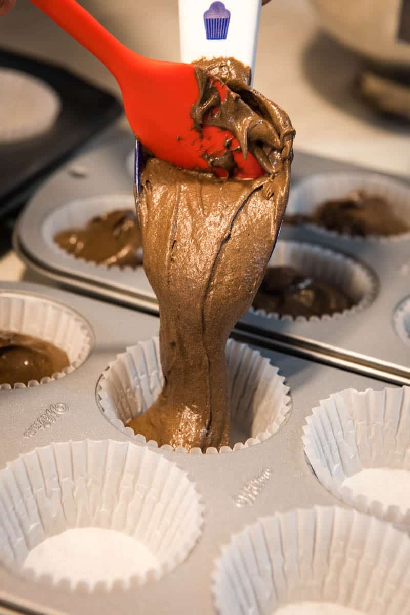 using white cupcake scoop to dispense chocolate cupcake batter into white cupcake liners in muffin tins