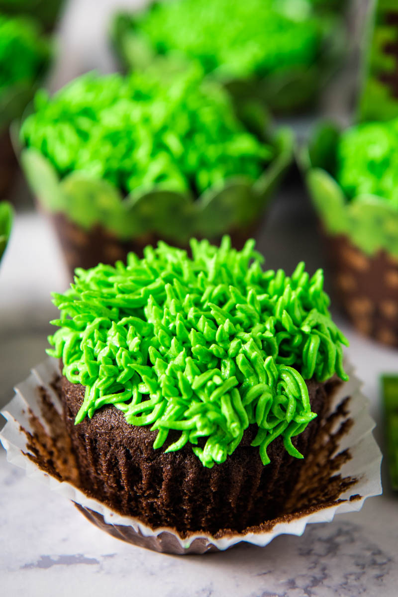 chocolate cupcake with green grass buttercream frosting, with white liner pulled away from cupcake