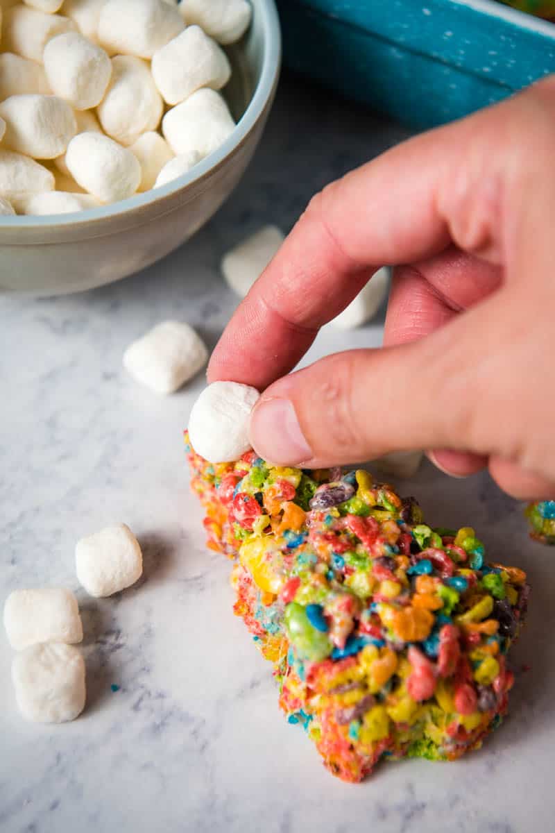 hand adding mini marshmallow star to Fruity Pebbles Christmas treats