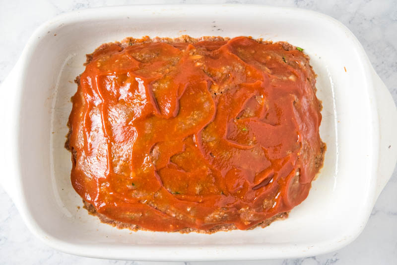 meatloaf sauce spread on top of meatloaf in white baking dish