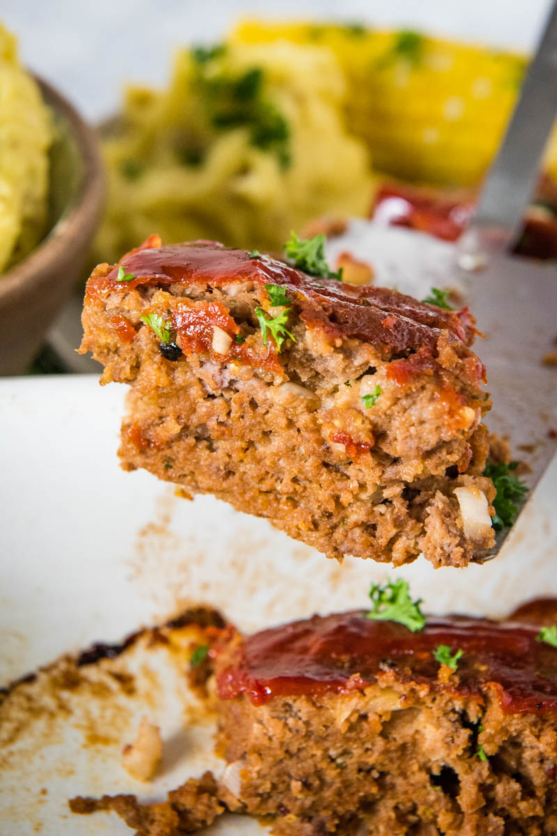 serving homemade meatloaf on spatula flipper over white baking dish