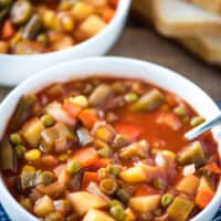 white bowl of CrockPot V8 vegetable soup with spoon on blue and white checked linen
