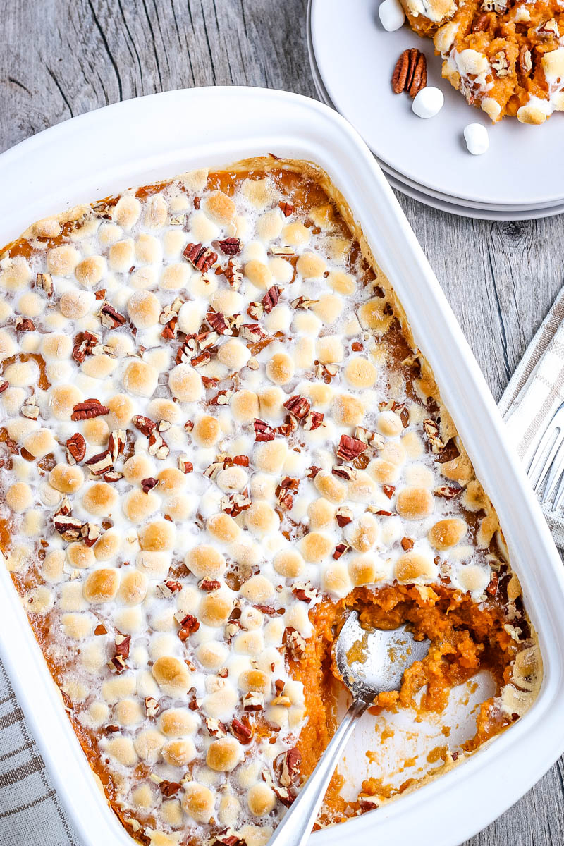 spoon scooping southern sweet potato casserole out of white baking dish and onto small white plate